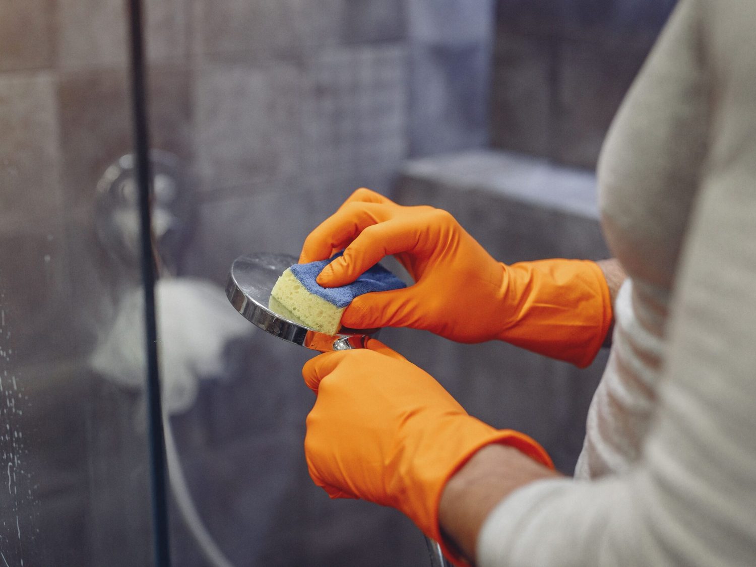 Crop faceless male in orange rubber gloves wiping by sponge shower nozzle